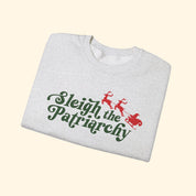 Folded gray sweatshirt with 'Sleigh the Patriarchy' text and reindeer graphics on a white background