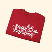 Folded red shirt with 'Sleigh the Patriarchy' text and graphic on a white background