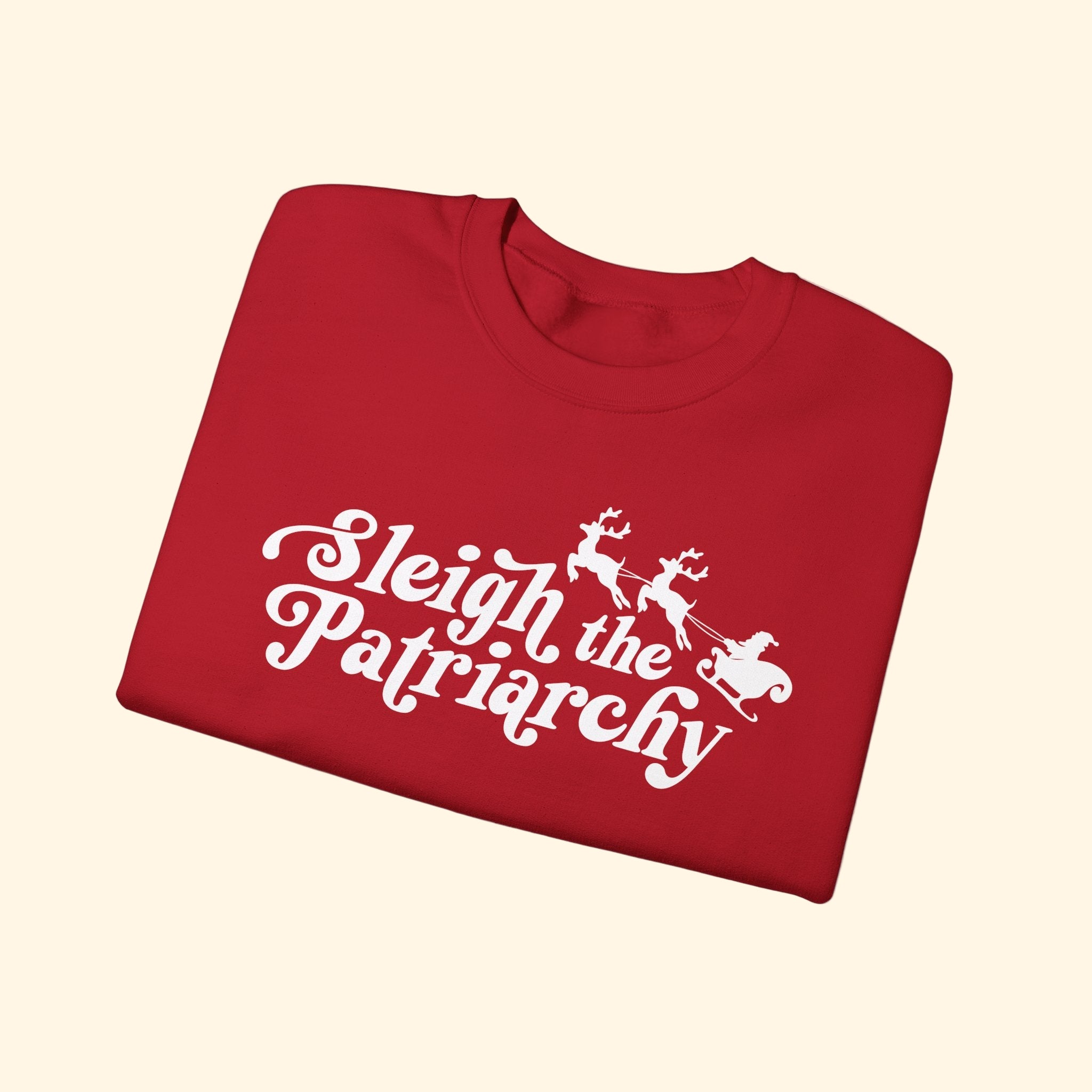 Folded red shirt with 'Sleigh the Patriarchy' text and graphic on a white background