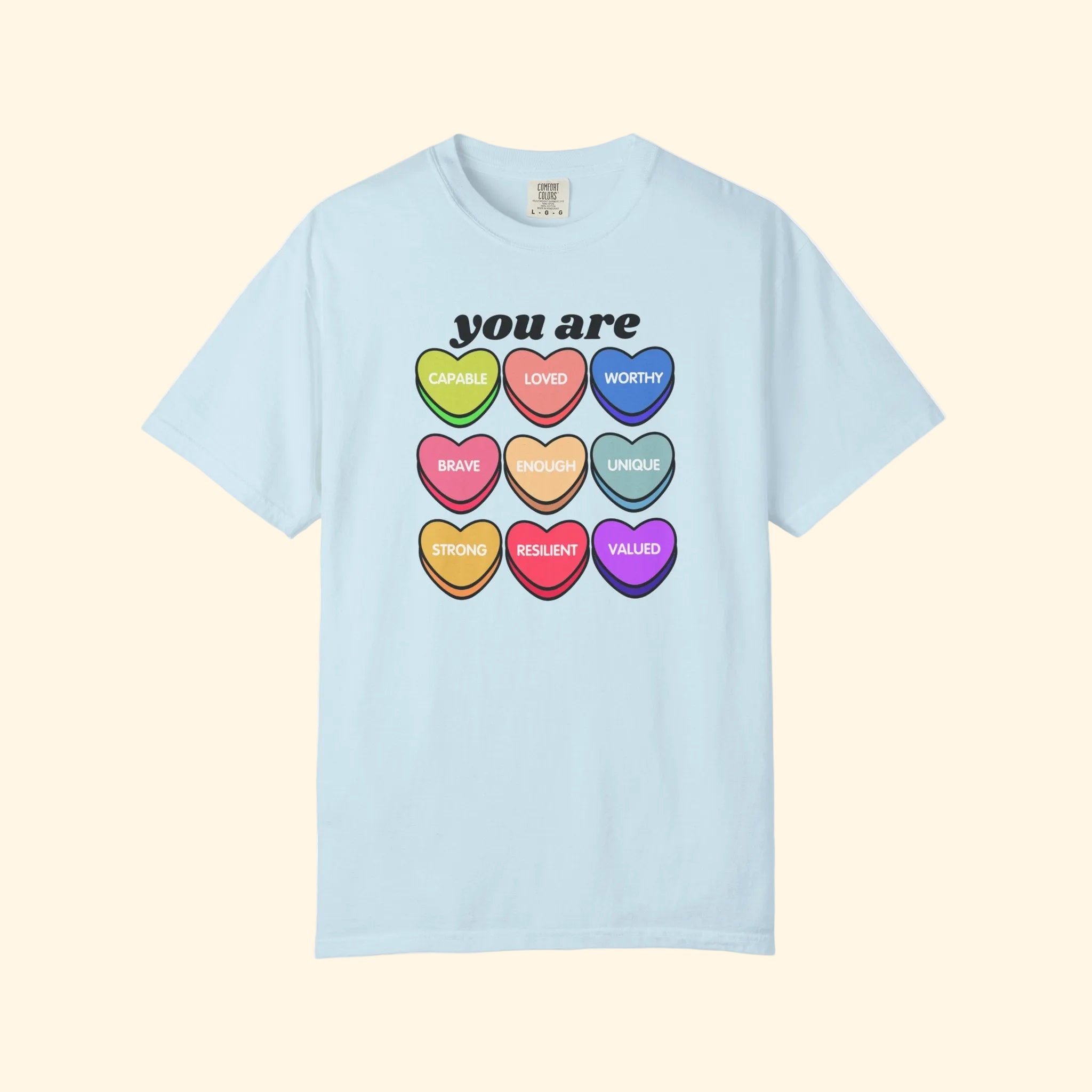 Light blue t-shirt with colorful heart-shaped affirmations on a white background