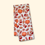 Folded towel with autumn-themed pattern featuring pumpkins and mugs on a beige background