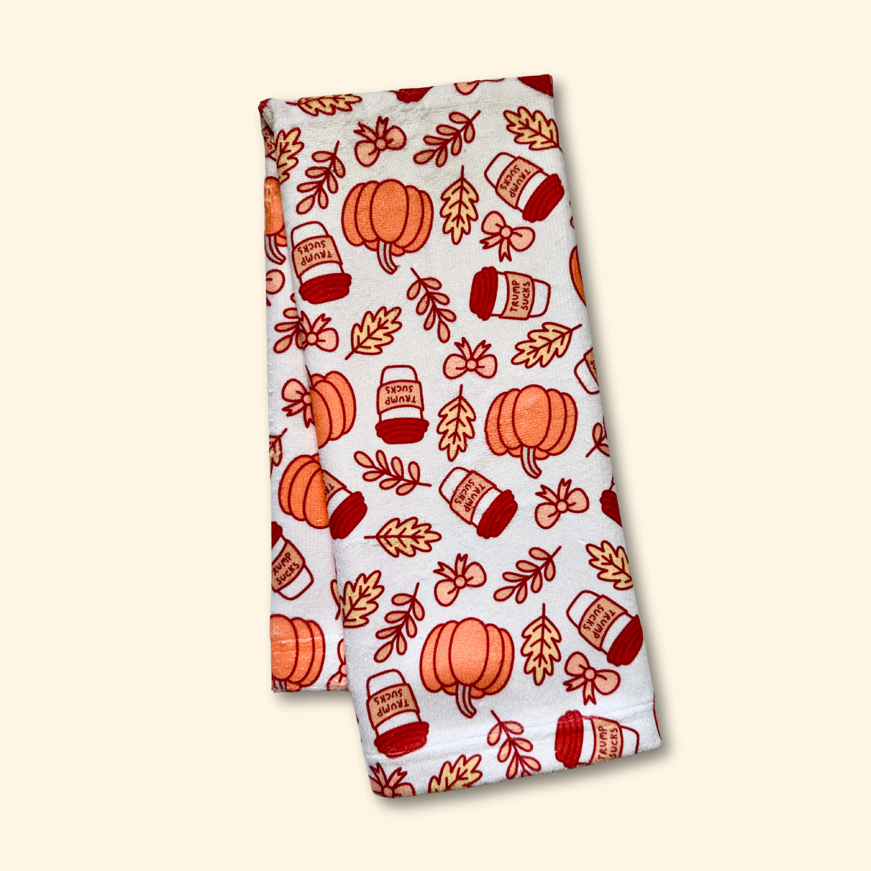 Folded towel with autumn-themed pattern featuring pumpkins and mugs on a beige background