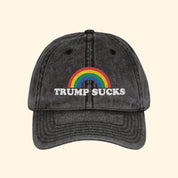 Black cap with rainbow and 'TRUMP SUCKS' text on a white background
