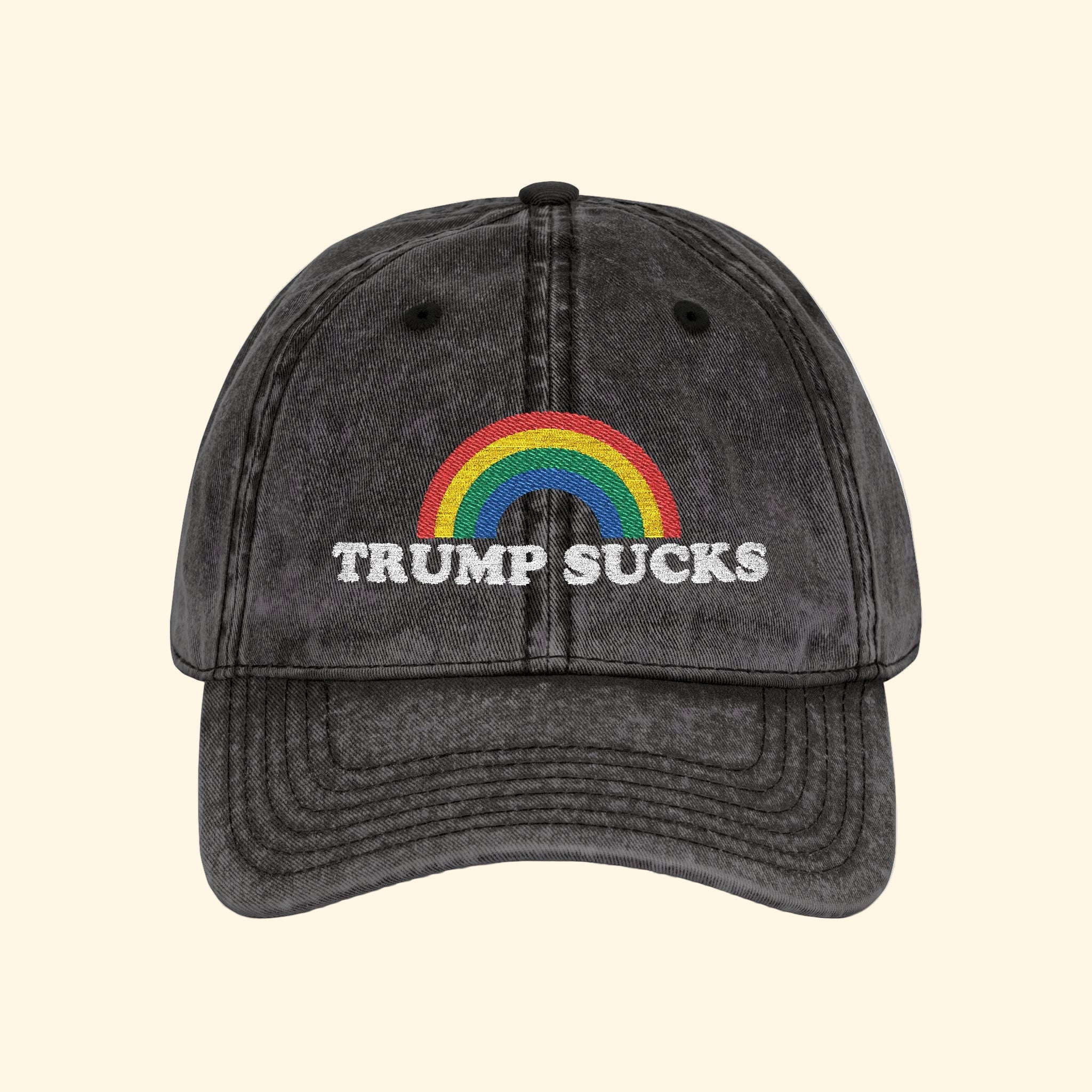 Black cap with rainbow and 'TRUMP SUCKS' text on a white background